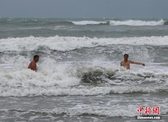 6月22日，海南三亚，游客在三亚湾冒险下海戏水。受今年第8号台风“鲸鱼”影响，三亚海边出现强风雨，海滩上大浪翻滚。中新社发尹海明摄