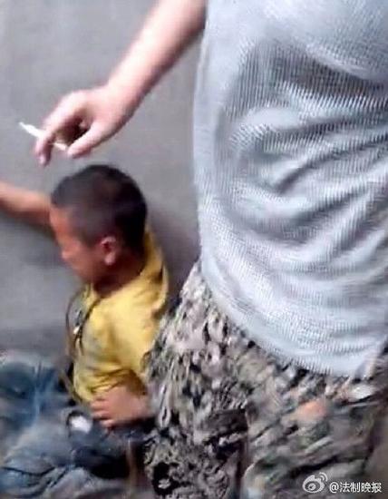 视频显示,该小学生遭到初中生暴力殴打。一初中生手持烟头,脚踩男童头部。 视频截图