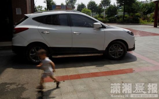 6月28日,湘潭华美丽都小区,出事的车子还停在小区里,一小朋友从车子边跑过。图/潇湘晨报记者华剑