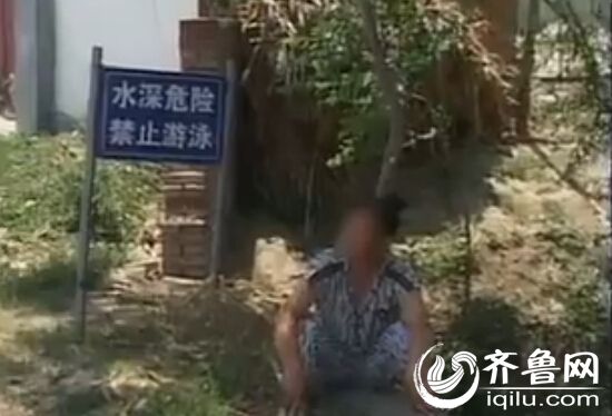 女子不但不开门,还从村北走到了村南头,坐在河边威胁执法人员。(视频截图)