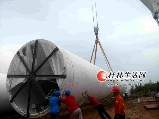 在西岭风电场9号坑位附近,重型吊机将塔筒从运输车上卸下。