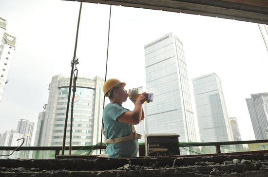 7月19日,成都市红星路二段,来自德阳的建筑工人李师傅乘坐吊篮车正在高温下作业,他每天要喝两大瓶茶水解渴。