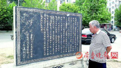 77岁的退休老支书房礼昌站在房家村的村碑前。