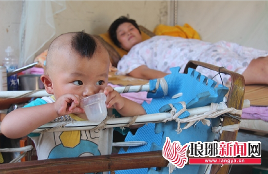 吳紅泥躺在床上望著兒子“天意”(11個(gè)月大),小天意安靜地待在爸爸自制的小推車?yán)铮T外。