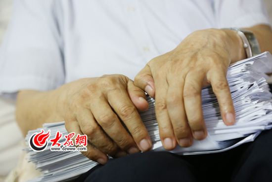 周加惠抱着他的厚厚的“支教记录”,此外,他还有厚厚的一摞外地来青学习的教师登记表,都像他的宝贝一样。(亓翔 摄)
