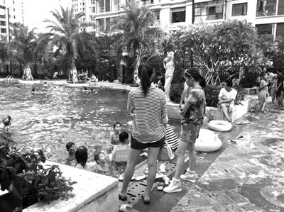 海口一小区的游泳池内，许多孩子在游玩，家长们在岸边陪护。