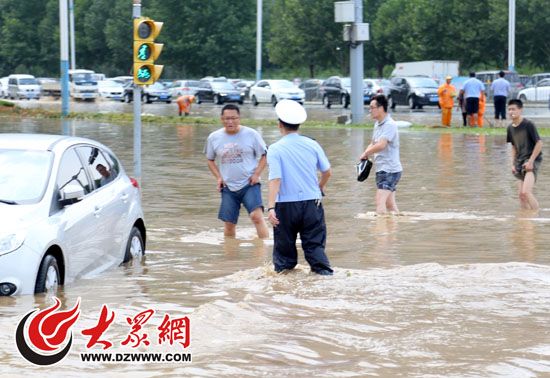 经十凤山路口积水严重，图中左侧轿车抛锚，市民正趟水过马路。