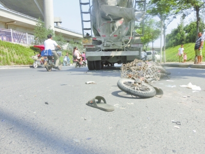 肇事的水泥罐車停在路口，車后有一攤血跡和一只男式拖鞋，地面上有大量的電動車碎片