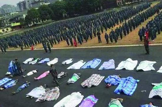 20多名女生躺在沥青跑道上，身上严严实实地裹着棉被，接受太阳的照晒