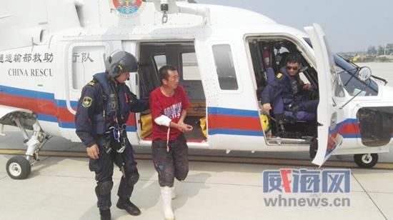救援人员护送断臂渔民下直升机。