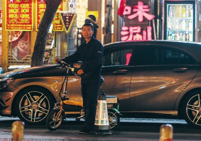 9月25日，一名代驾在簋街的饭店门口“等活”，小折叠车是代驾的必备装备。