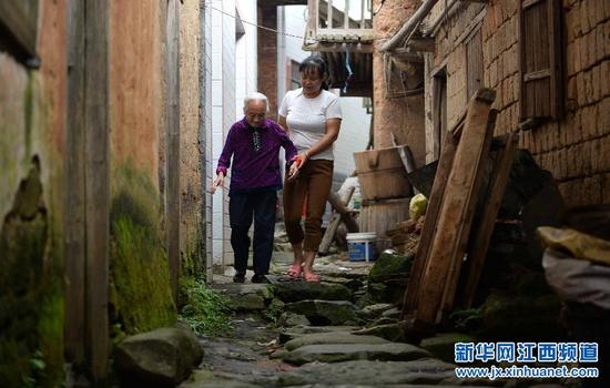 在广昌县塘坊乡横山村，袁菊兰扶着婆婆骆金秀走出家门散步。在与现任丈夫谢维才结婚后，袁菊兰一家搬到了条件较好的住处。然而近几年，年事已高的婆婆希望回到老家度过晚年，袁菊兰和谢维才便陪着老人搬回了房屋、路况条件都较差的老家（9月26日摄）。
