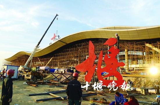 施工人員正在吊裝兩個(gè)巨型紅色大字——“十堰”。