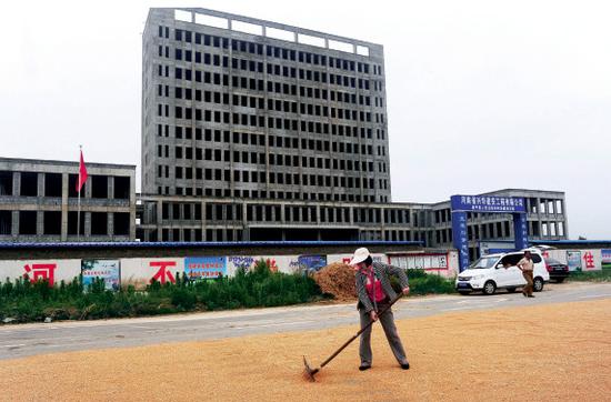 2014年5月27日，河南省驻马店市，农民在停工的遂平县法院大楼边晒麦子。