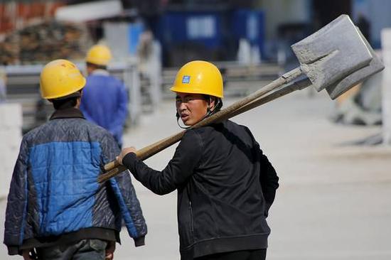 2015年10月15日,北京,一名扛着铁铲的工人经过一条道路的施工工地.