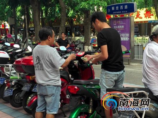 海口市解放西路多宝利商业广场前电动车停放点仍有人在向停车市民收取两元停车费，周围并未看到任何电动车停放收费标识和收费标准公告牌。(南海网记者周静泊摄)