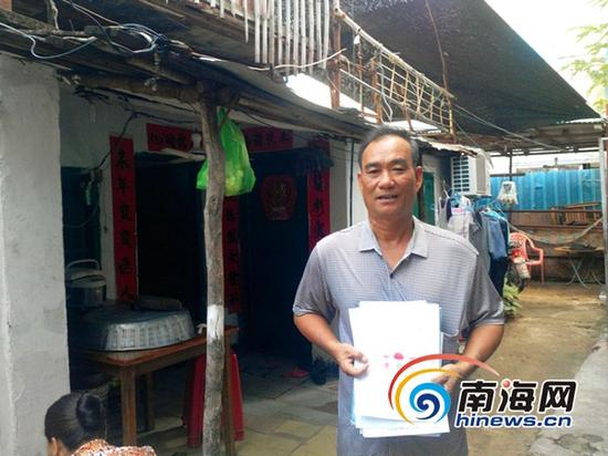 居民李良拿着相关材料站在自己已居住30多年的老屋前(南海网记者刘培远摄)