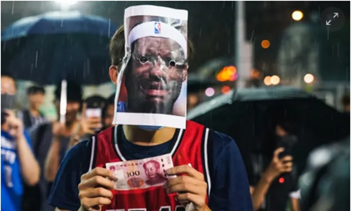 示威者头戴詹姆斯纸片面具，手持人民币。来源：《卫报》
