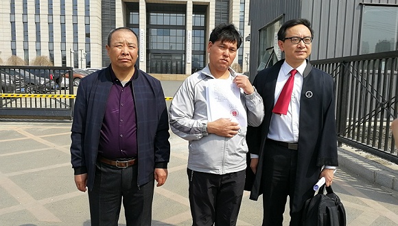 刘忠林拿着无罪判决书，和表姐夫王贵贞以及律师张宇鹏在法院门口。界面新闻记者 黄丽君摄
