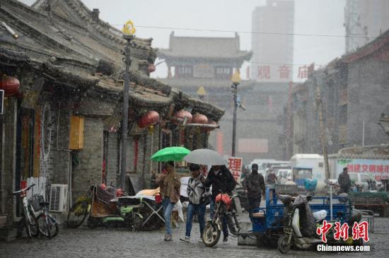 4月3日,雪中的明清古街,民众撑伞步行。当日,呼和浩特迎来降雪,气温骤然下降,不少民众纷纷加衣保暖。中新社记者 刘文华 摄
