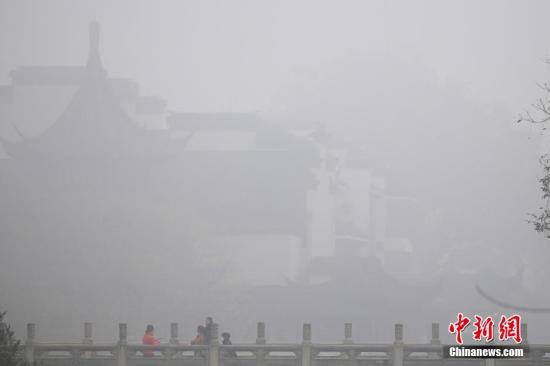 12月21日，市民从被雾气笼罩的夫子庙景区内经过。当日清晨，江苏省气象台发布大雾橙色预警信号，受大雾影响，部分地区能见度小于200米、局部地区能见度小于50米，多条高速被关闭。 泱波 摄