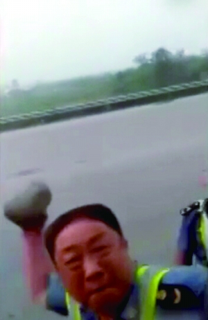 视频中一名穿制服男子拿起大块石头砸车窗玻璃。视频截图