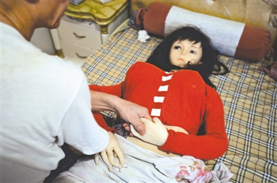 张先生拉着实体娃娃的手和它聊天，寄托对妻子的哀思