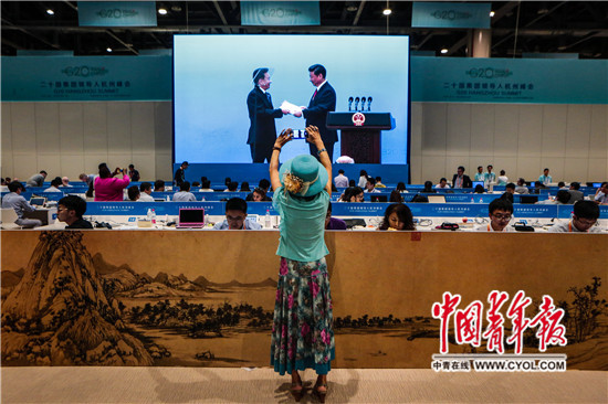 2016年9月3日，G20杭州峰会新闻中心，一名外媒记者在用手机拍照。前方大屏幕正直播B20主席、中国贸促会会长姜增伟代表工商界向习近平主席递交《2016年B20政策建议报告》，该报告为G20峰会提出了20项政策建议。中国青年报·中青在线记者 赵迪/摄