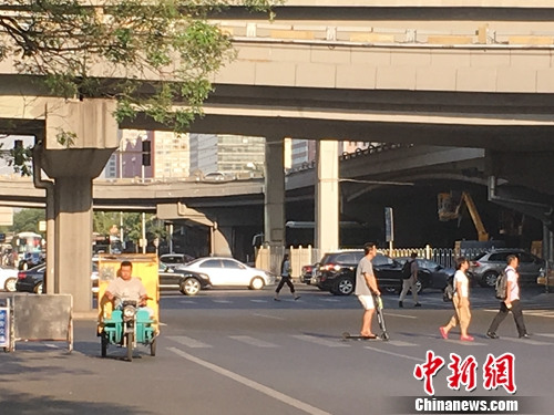 北京國貿附近有人騎電動滑板車過馬路。湯琪 攝