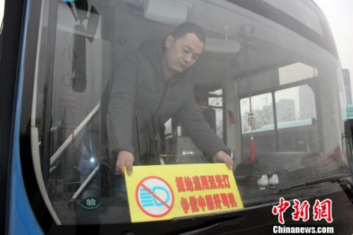 资料图：一名郑州4路公交车车长将印有“拒绝滥用远光灯争做中国好司机”的宣传展板放在车辆前挡风玻璃上，时刻提醒自己文明行车。 周小云 摄