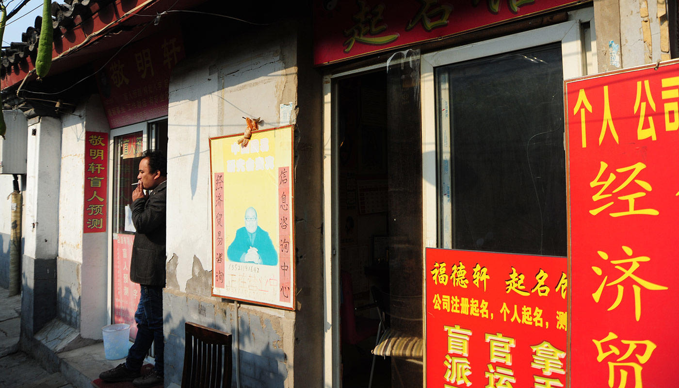1 雍和宫大街人行道上总停着一辆公务三轮车,车把挂个大喇叭,功放着告示:看相,算命,起名,都是骗人行为,提醒广大游客不要上当受骗。一遍又一遍循环。 街上路窄车多,人来人往。因为雍和宫的关系,沿街有许多佛具用品店,唵嘛呢叭咪吽的佛乐没完没了播放,路上有时弥散着香火气。午间到傍晚,两侧人行道上常有个把穿着灰暗、跨个包、揣着手的中老年人,站在路边张望。你走过时,一张神色幽深的脸就凑到面前,姑娘,我看你面相不错。 他们都是散户,真正的风水大本营在路西侧的国子监街,穿过那面红柱蓝面、雕饰华丽的成贤街