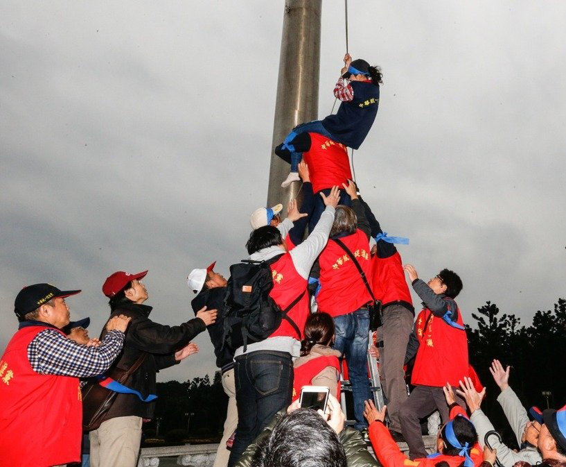  岛内的中国统一促进党支持者，将中正纪念堂前广场上的“半旗”升起。馆方派人将旗再次降下，统一党支持者再次拿梯子爬上去将旗升上。（图片来源：台湾联合新闻网）