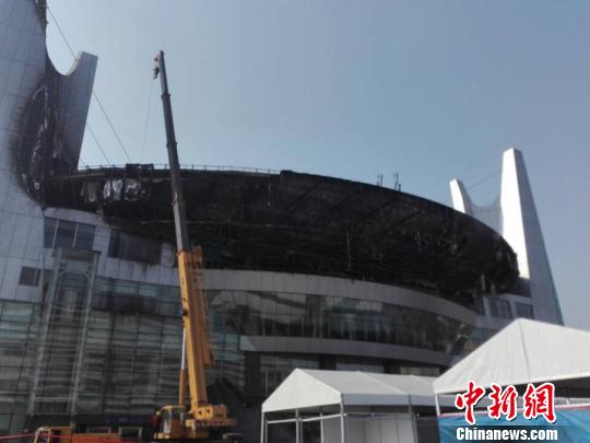 图为27日早上,记者在被扑灭的大火现场看到,体育中心北大门中间以上大型外观面弧形部位至外观点最高处内部钢架已裸露在外。 王祎 摄