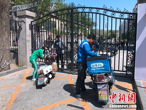 2017年4月21日，北京交通大学南门附近，由于快递电动车无法进入校园，一名学生隔着铁门取外卖。潘心怡 摄