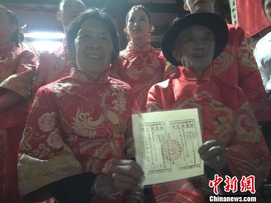 5月1日,客家聚居地江西省瑞金市举办首届客家集体婚礼,来自福建、江西等地的百对新人在此体验下轿鸡、跨火盆、过米筛、金称挑盖头等客家婚礼习俗。图为91岁的刘先树和81岁的钟美英金婚夫妇喜获一张写有两人名字的“苏区时期的结婚证”。 苏路程 摄