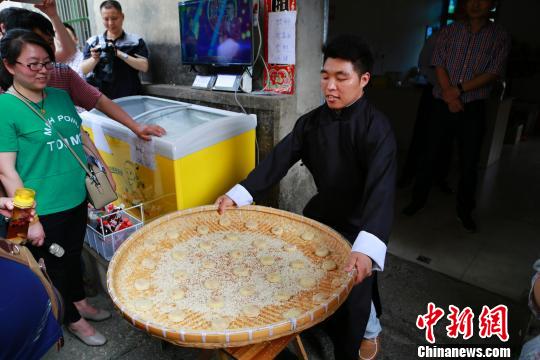 图为:浙江省江山市廿八都“古镇麻饼”传承人王庭高正在向游客演示技艺。便利的京台高速、205国道,带火了这个隐于高山深谷中的古镇,让当地传统手工艺有了复兴传承的机会。 王远 摄
