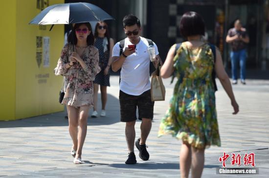 图为北京三里屯街头市民撑伞遮阳。 <a target=\'_blank\' href=\'http://www.chinanews.com/\' >中新网</a>记者 金硕 摄