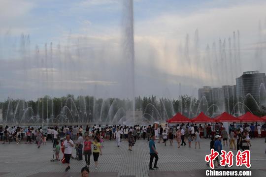 傍晚时分,游客在新疆克拉玛依河边观看喷泉。 袁晶 摄