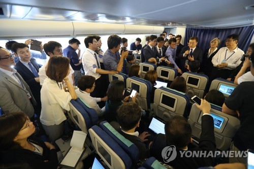  6月28日下午，韩国总统文在寅（居中，手拿麦克风）在专机上回答记者提问。（韩联社）