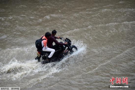 资料图:印度进入雨季,民众骑摩托车经过被大水淹没的街道。