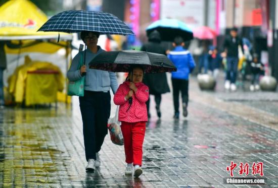 资料图:9月24日,新疆乌鲁木齐市降下秋雨,外出民众打着雨伞快步前行。 中新社记者 刘新 摄