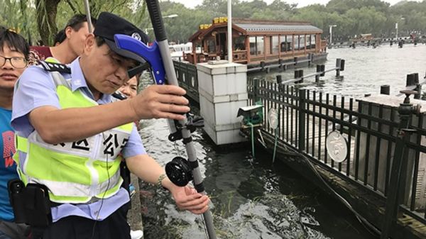 周翔军警官用他自制的工具帮助游客打捞掉进西湖里的手机(香港《南华早报》网站)