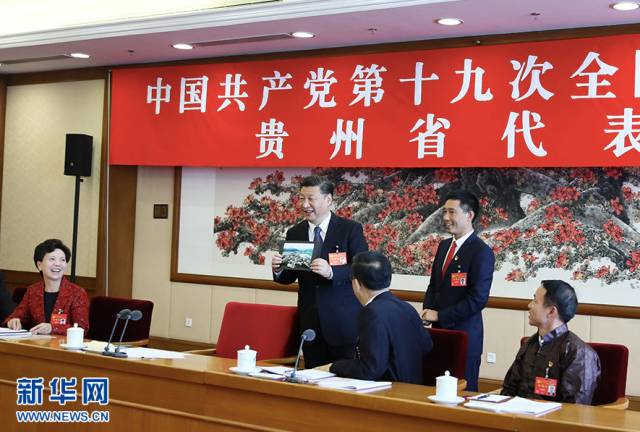  10月19日，习近平同志参加党的十九大贵州省代表团讨论。这是遵义市播州区花茂村党总支书记潘克刚将一幅鸟瞰村子新貌的照片送到习近平面前。习近平起身接过照片，边看边称赞：“这是风景画，很漂亮！” 新华社记者 兰红光 摄