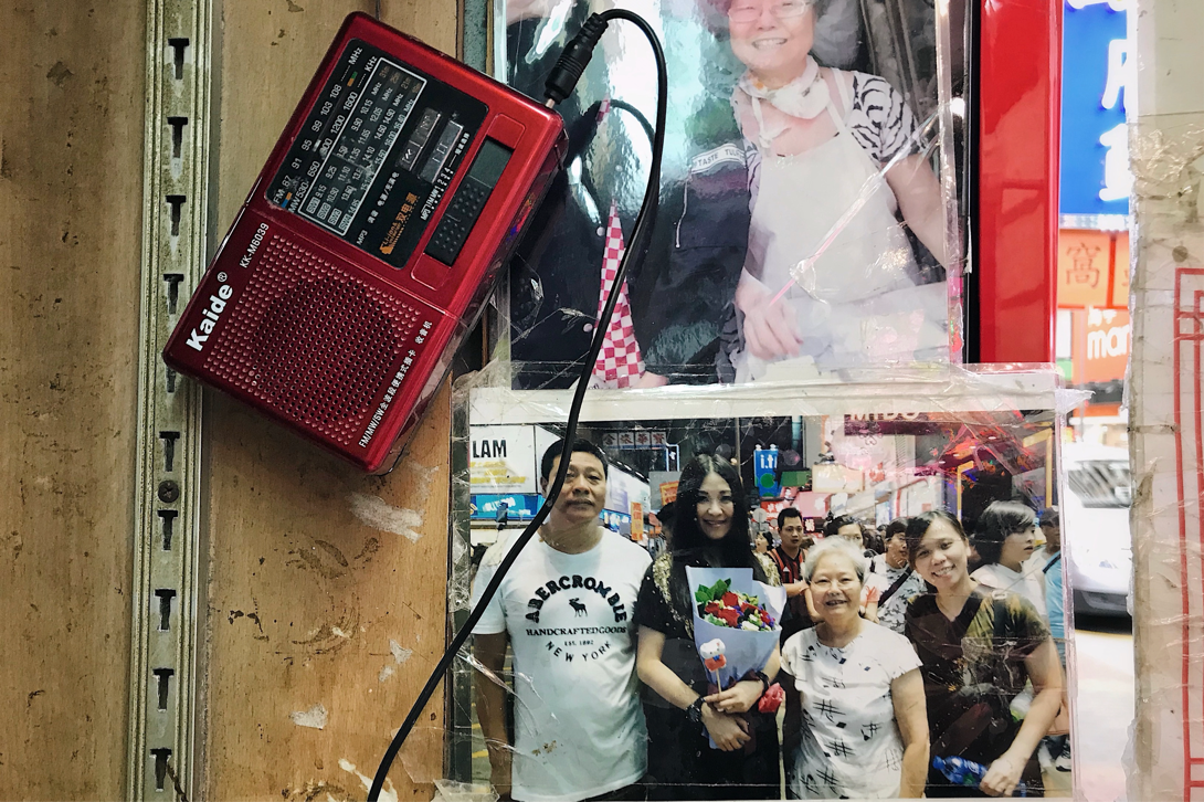 余太龙须酥摊位旁的墙壁上挂的红色收音机，还有她与彭梓嘉的合影。