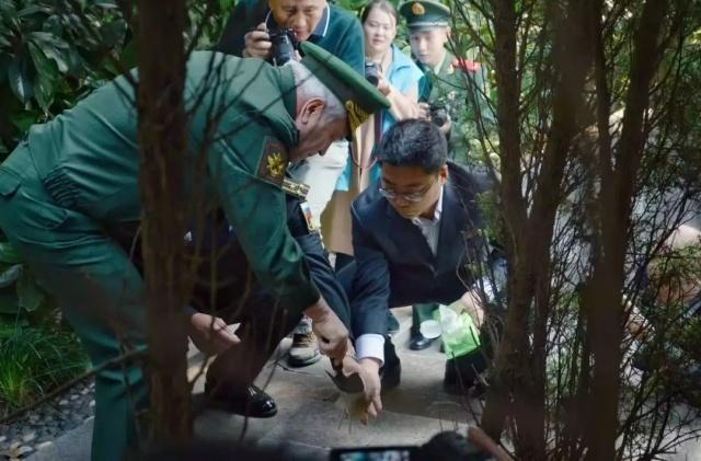 俄罗斯联邦国防部副部长潘科夫(左一)在烈士墓地采集泥土装入布袋,记者谌达军(右一)一旁协助。 陈文君摄