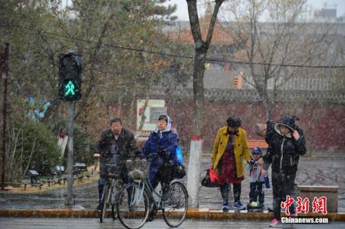 4月3日，民众在雪中步行过马路。当日，呼和浩特迎来降雪，气温骤然下降，不少民众纷纷加衣保暖。中新社记者 刘文华 摄