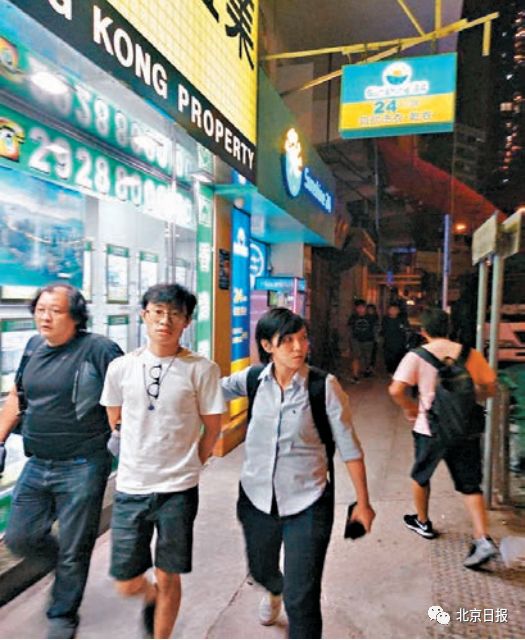 其中一名涉案青年（白衫），由探员押解到大 角咀一单位搜证。来源：香港《文汇报》