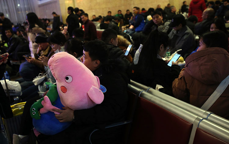 北京站候车室一位男乘客怀中抱着一只“小猪”毛绒玩具，这是准备春节回家送给女朋友的。