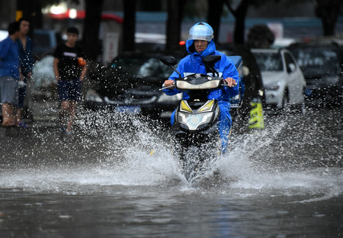 7月16日，一名快餐配送员从北京西城区一段积水的路面骑过。新华社记者 罗晓光 摄