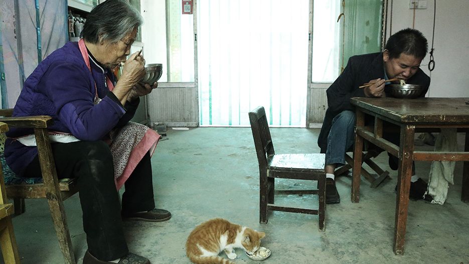 一家人在吃烩面,保山金山手臂无力端不起碗,只能趴在桌子上,用筷子挑着吃。